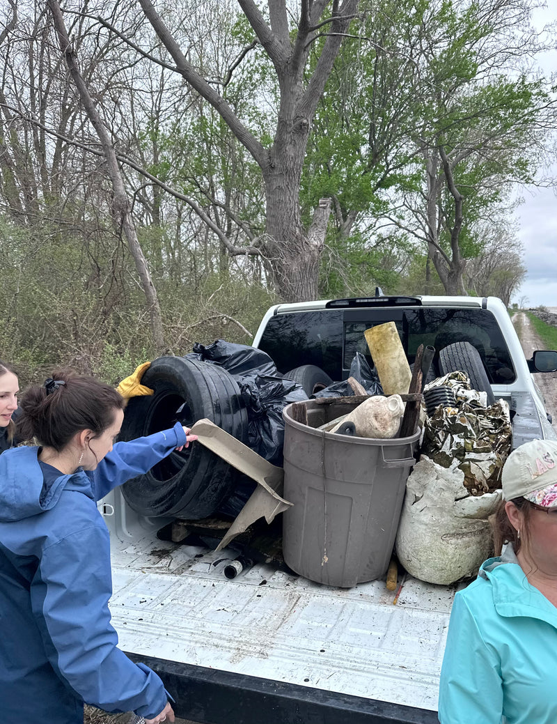 Two people loading trash in a truck bed with trees and a cloudy sky in the background