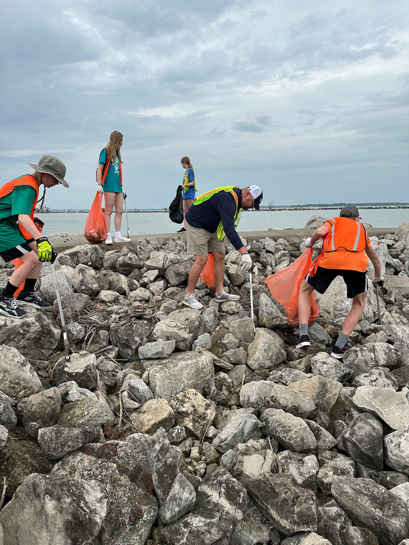 People cleaning up a rocky Lake Erie shoreline with orange bags on a cloudy day.