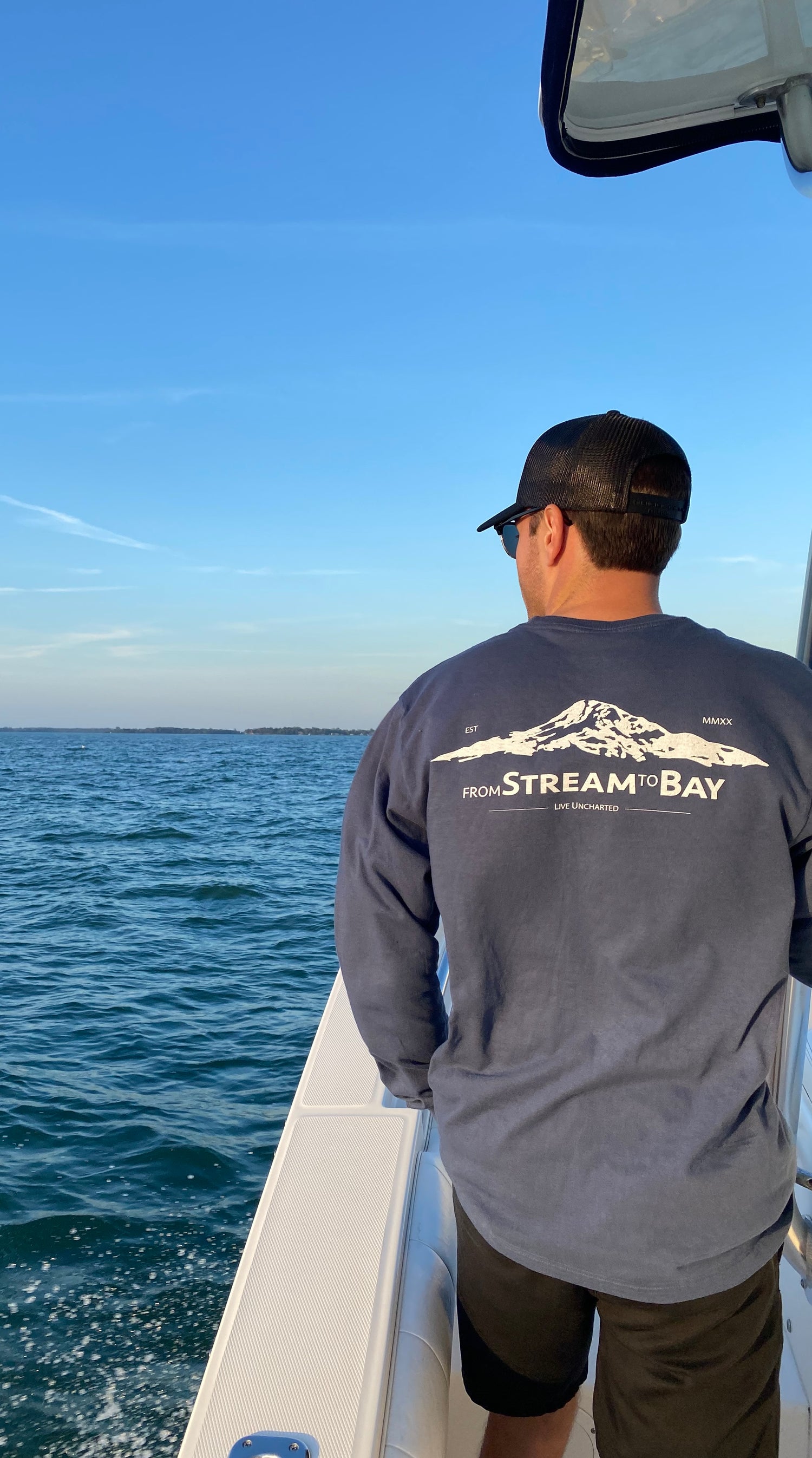 Man on a boat wearing a shirt with 'from Stream & Bay' logo, looking at the ocean.