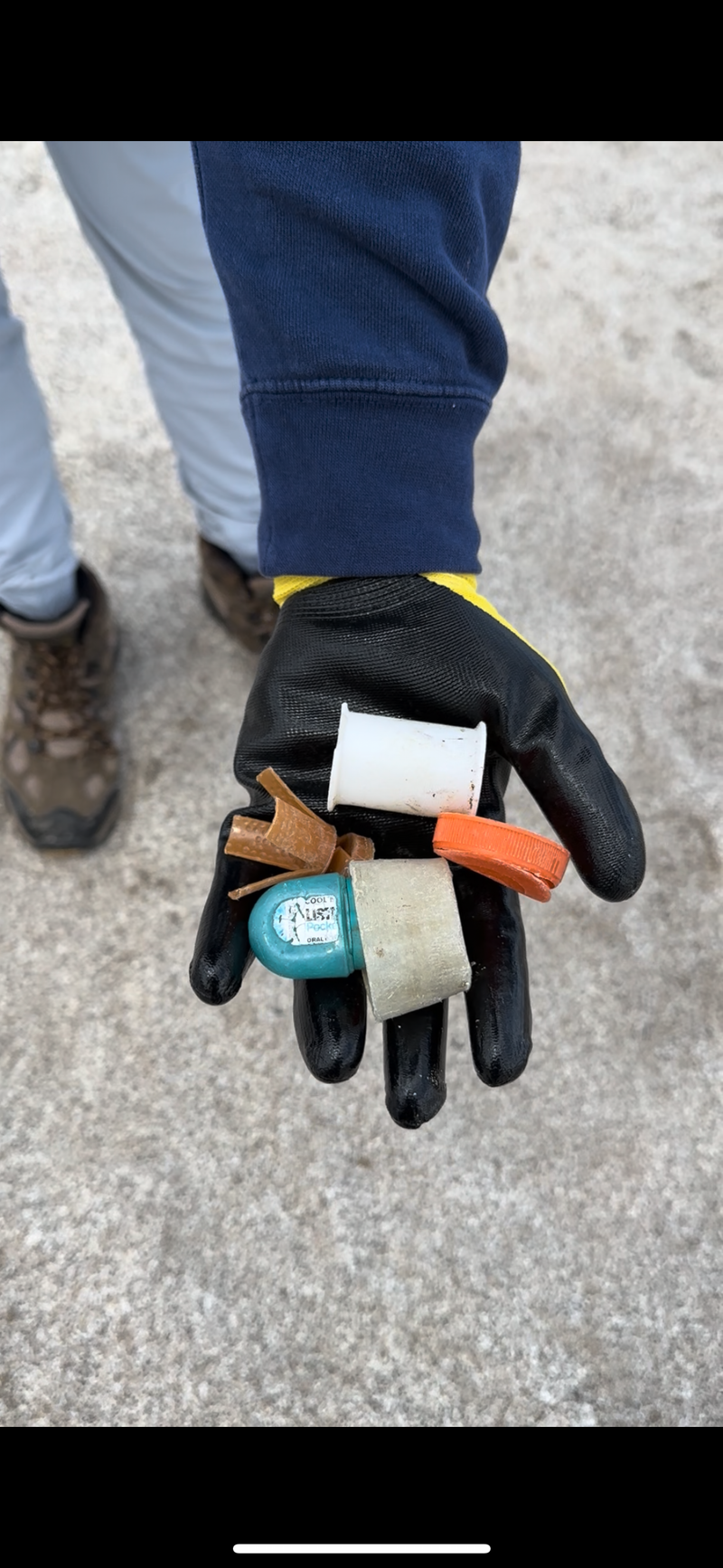 Hand wearing a black glove holding small pieces of trash on a beach
